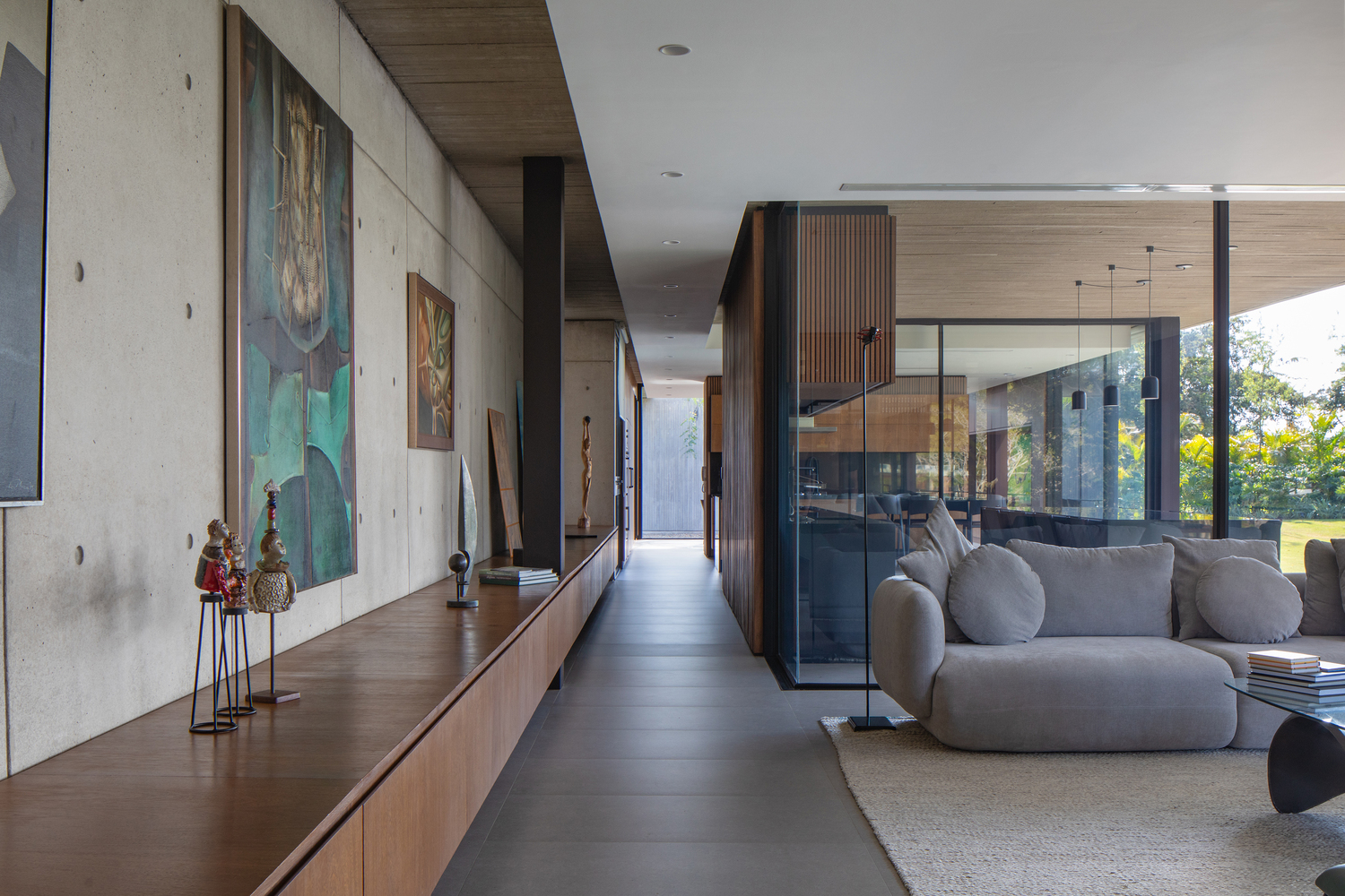 Интерьер открытой гостиной-галереи с бетонной стеной, искусством и видом на сад