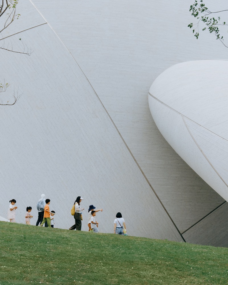 Травяной склон у гладкого белого фасада с группой гуляющих детей